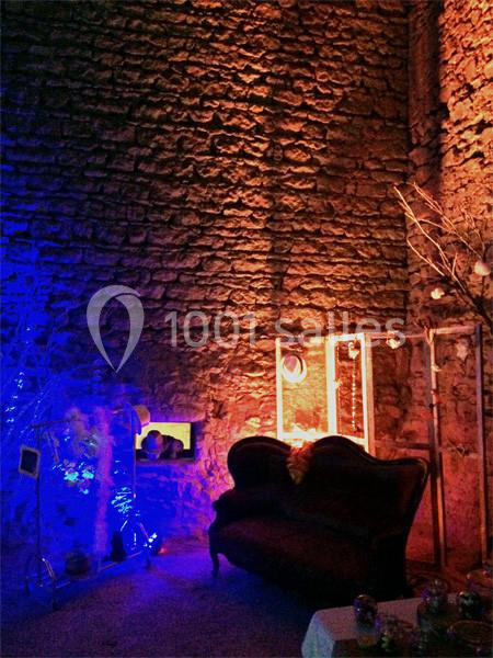 Mur en pierre éclairé par des lumières colorées, avec un canapé ancien et des éléments décoratifs.