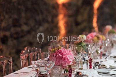 Scooter rose décoré de fleurs roses et blanches, stationné près d'un mur en pierre et d'une porte en bois.