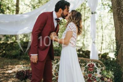 Scooter rose décoré de fleurs roses et blanches, stationné près d'un mur en pierre et d'une porte en bois.