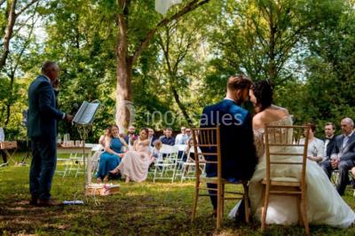 Scooter rose décoré de fleurs roses et blanches, stationné près d'un mur en pierre et d'une porte en bois.