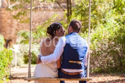 Scooter rose décoré de fleurs roses et blanches, stationné près d'un mur en pierre et d'une porte en bois.