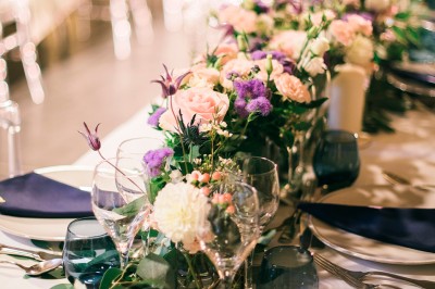 Scooter rose décoré de fleurs roses et blanches, stationné près d'un mur en pierre et d'une porte en bois.