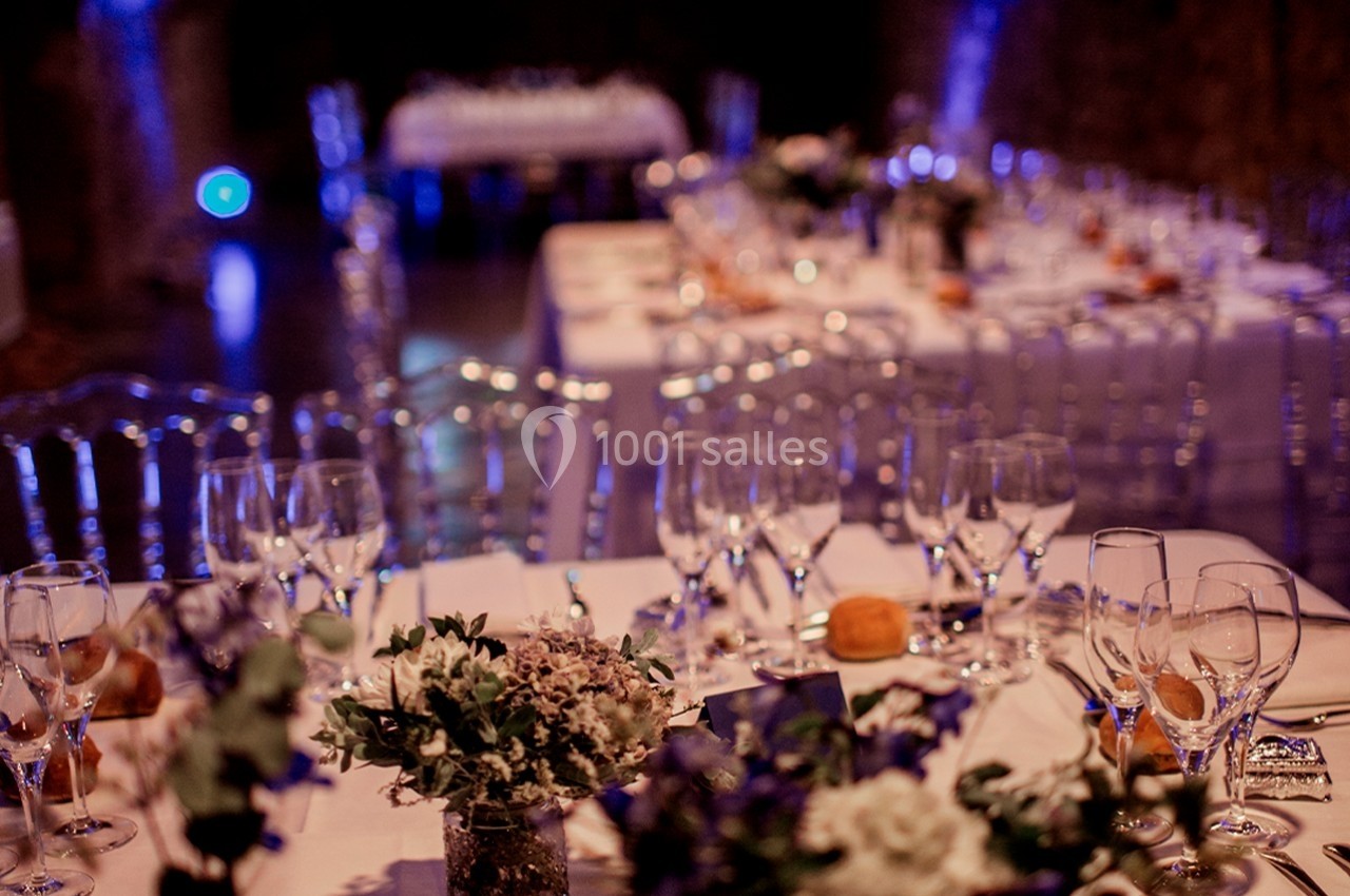 Tables décorées avec des fleurs et des verres en cristal dans une salle éclairée d'une lumière tamisée.