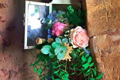 Scooter rose décoré de fleurs roses et blanches, stationné près d'un mur en pierre et d'une porte en bois.