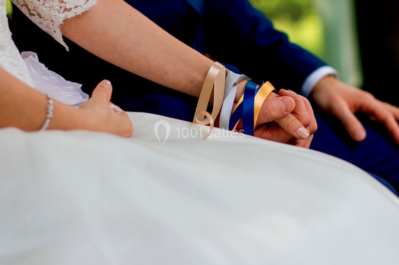 Deux mains entrelacées, entourées de rubans colorés, lors d'une cérémonie de mariage.