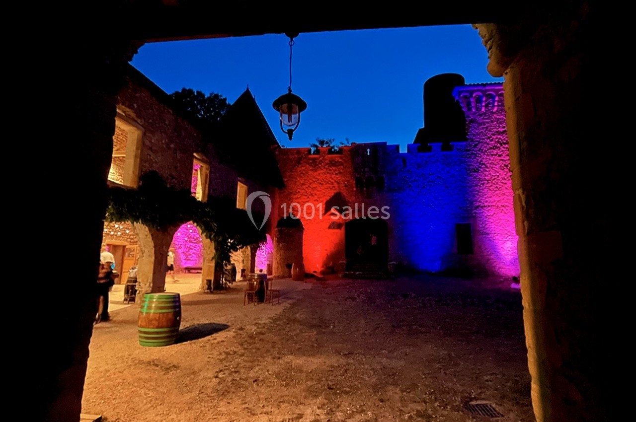 Cour intérieure d'un château éclairée par des lumières colorées, avec un ciel nocturne en arrière-plan.