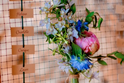 Scooter rose décoré de fleurs roses et blanches, stationné près d'un mur en pierre et d'une porte en bois.