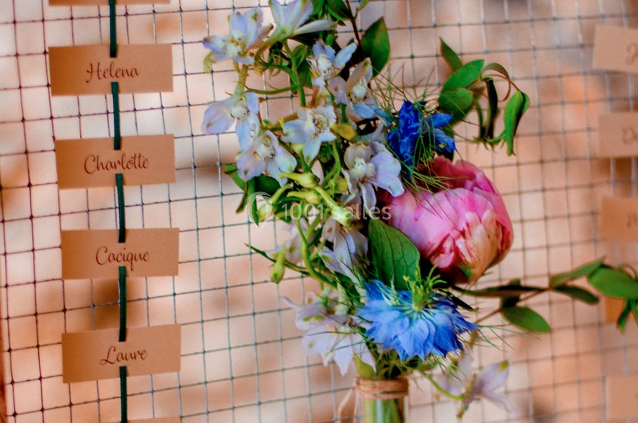 Bouquet de fleurs colorées avec des étiquettes de noms suspendues sur un fond de grille métallique.