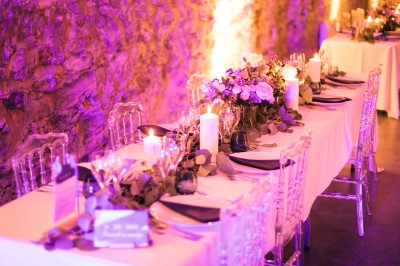 Scooter rose décoré de fleurs roses et blanches, stationné près d'un mur en pierre et d'une porte en bois.