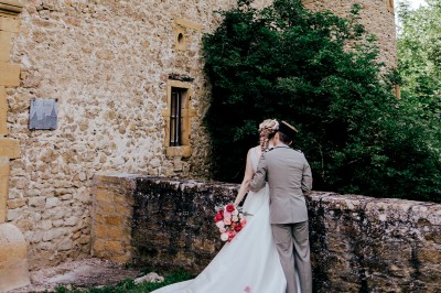 Scooter rose décoré de fleurs roses et blanches, stationné près d'un mur en pierre et d'une porte en bois.