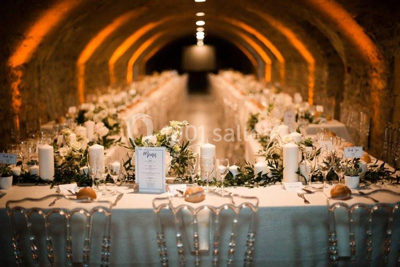 Table décorée pour un dîner élégant dans une salle voûtée, ornée de bougies, fleurs blanches et vaisselle raffinée.