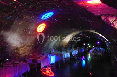 Scooter rose décoré de fleurs roses et blanches, stationné près d'un mur en pierre et d'une porte en bois.