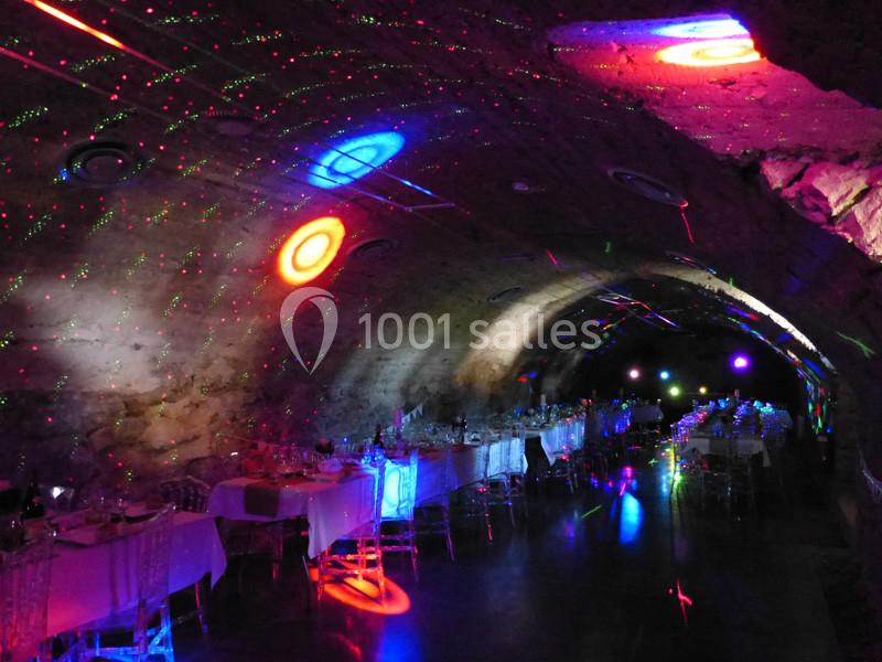 Salle voûtée éclairée par des lumières colorées, avec des tables dressées pour un événement.