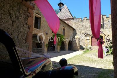 Scooter rose décoré de fleurs roses et blanches, stationné près d'un mur en pierre et d'une porte en bois.
