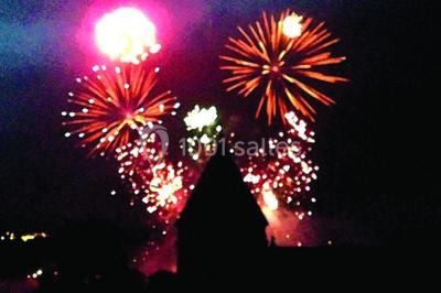 Scooter rose décoré de fleurs roses et blanches, stationné près d'un mur en pierre et d'une porte en bois.