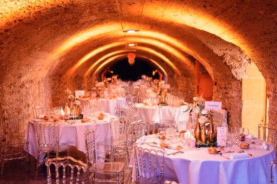 Scooter rose décoré de fleurs roses et blanches, stationné près d'un mur en pierre et d'une porte en bois.