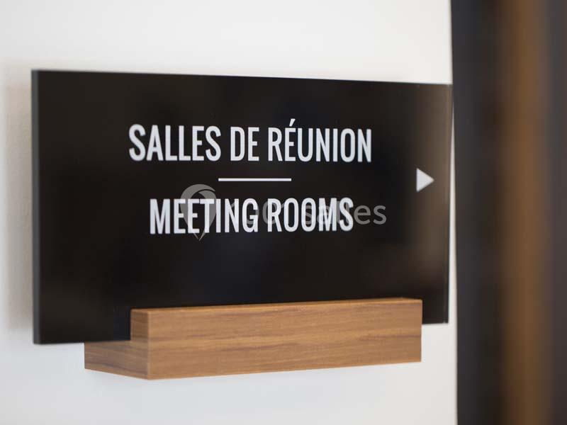 Panneau indiquant des salles de réunion en français et en anglais, fixé sur un support en bois.