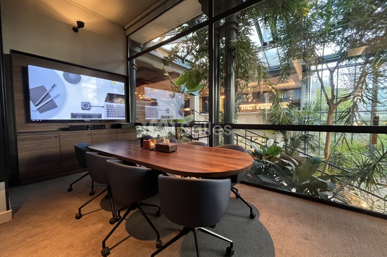 Salle de réunion moderne avec table en bois, chaises noires et grande baie vitrée donnant sur un espace végétalisé.