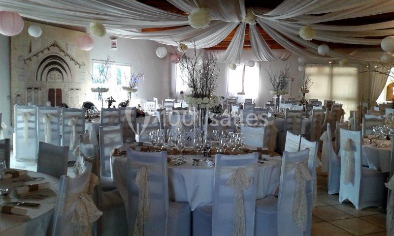 Salle de réception décorée avec des tables rondes, nappes blanches, chaises habillées et guirlandes suspendues.