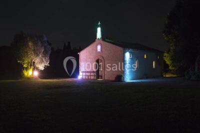 Petite chapelle en pierre éclairée par des lumières colorées dans un environnement nocturne.