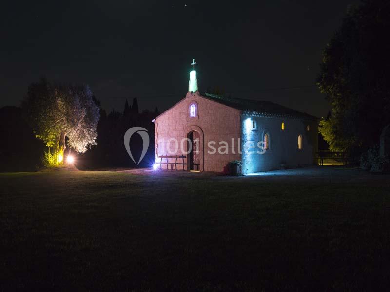 Petite chapelle en pierre éclairée par des lumières colorées dans un environnement nocturne.
