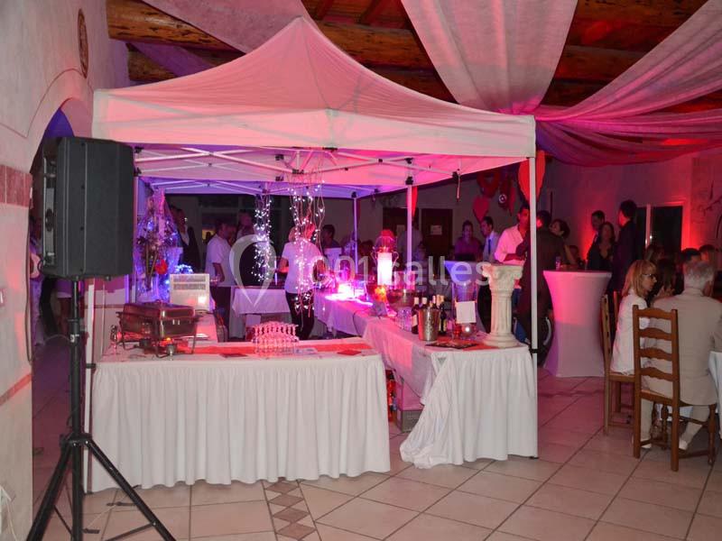 Stand de buffet décoré sous une tente blanche dans une salle éclairée par des lumières colorées, avec des invités en arrière…
