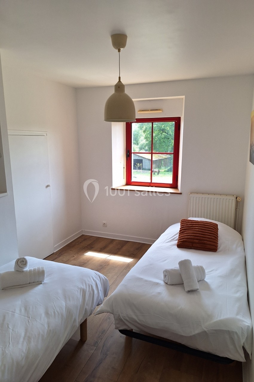 Chambre lumineuse avec deux lits simples, parquet, fenêtre donnant sur un jardin et décoration minimaliste.
