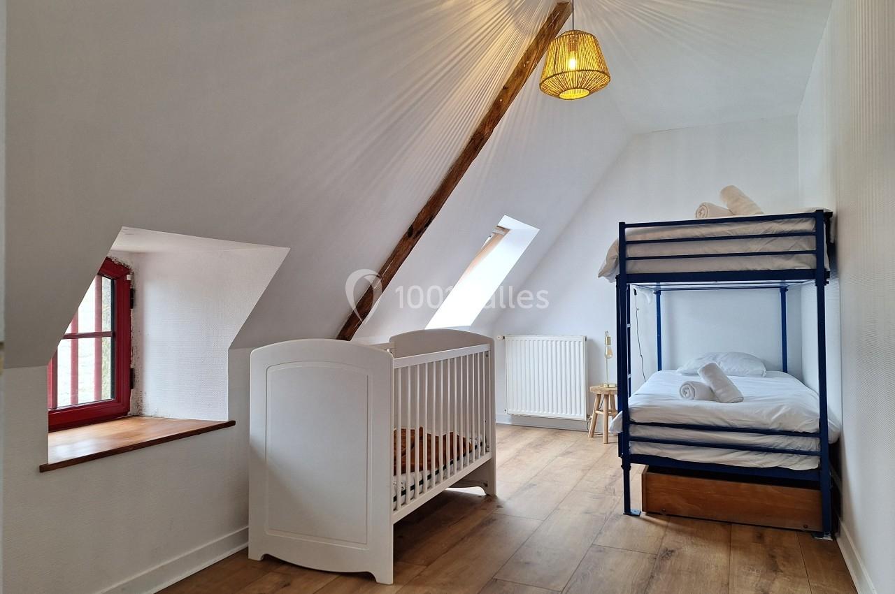 Chambre mansardée avec lit superposé, lit bébé, fenêtre à battants et parquet clair.