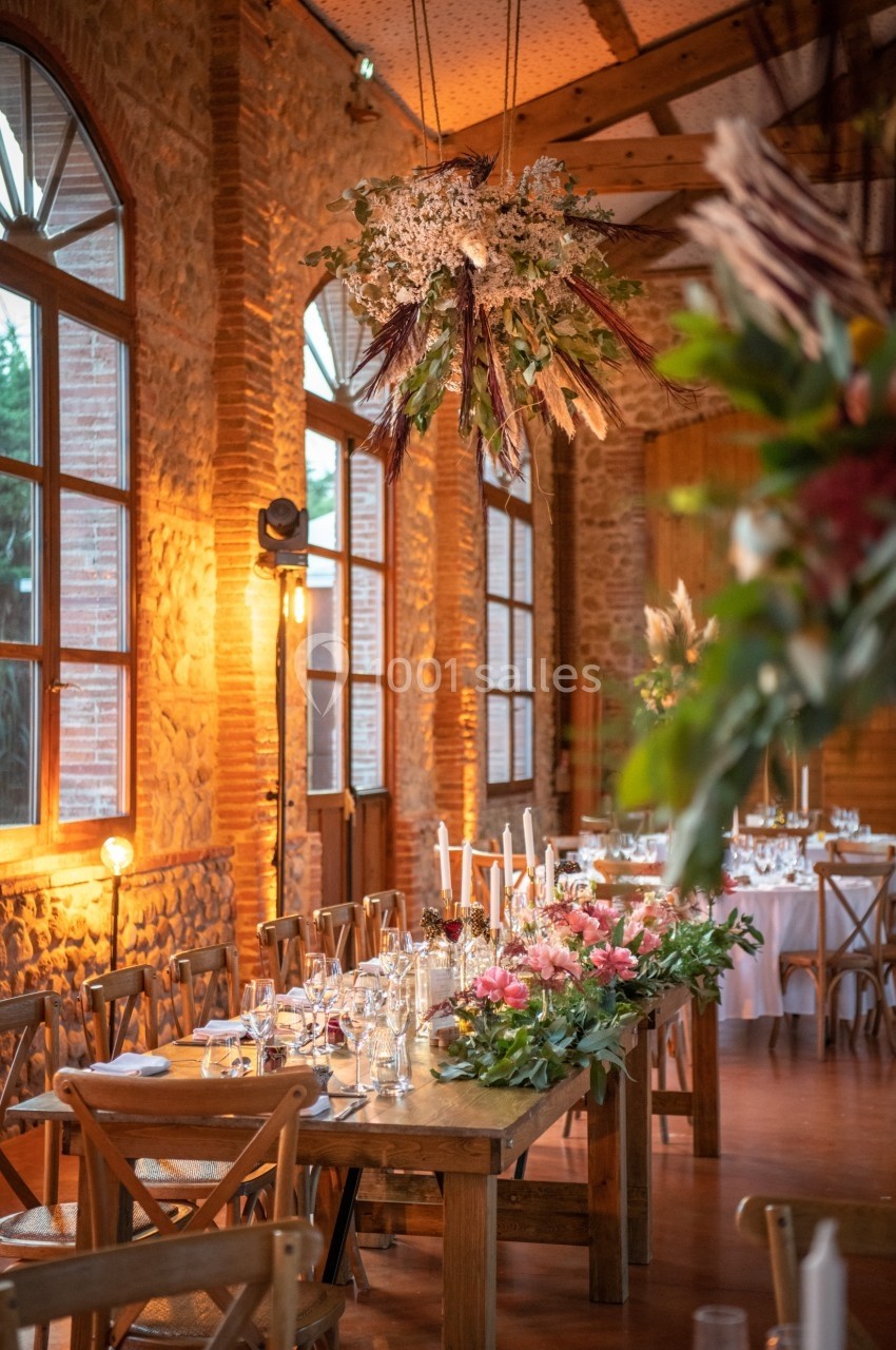 Salle de réception décorée avec des fleurs, des tables en bois dressées et une ambiance lumineuse chaleureuse.