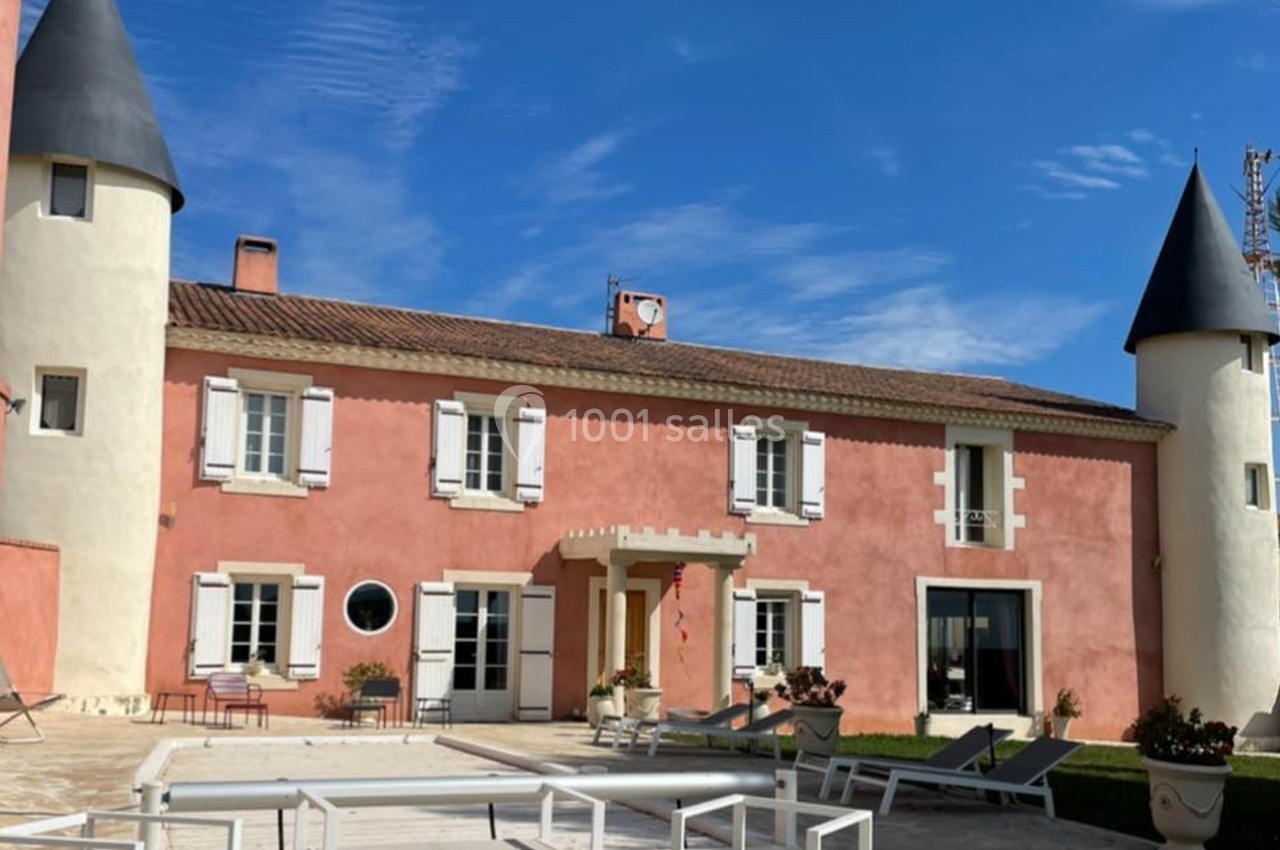 Façade d'une maison rose de style château avec deux tours, entourée d'une terrasse et de mobilier extérieur.