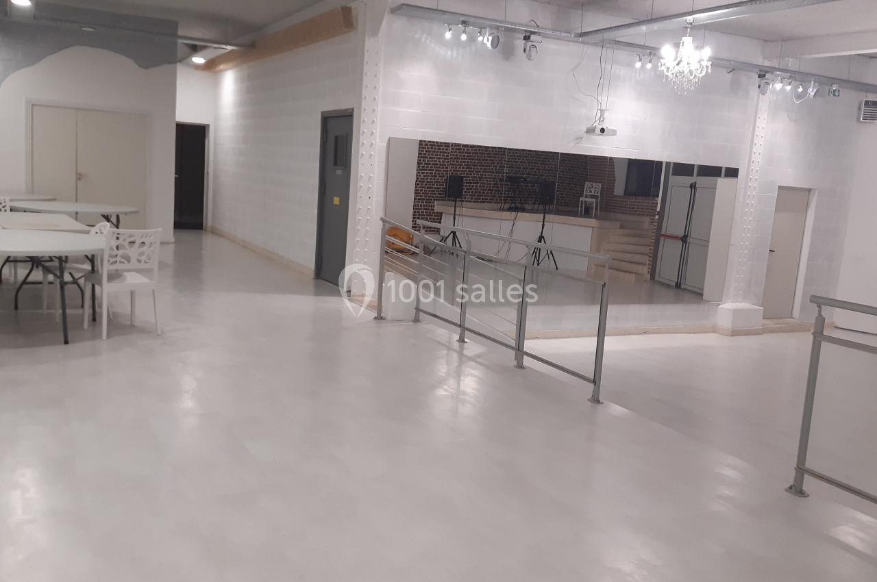 Location salle Tourcoing (Nord) - Latin Dance #2 Salle lumineuse avec sol clair, tables, chaises blanches, miroir mural, rampe d'accès et éclairage suspendu.