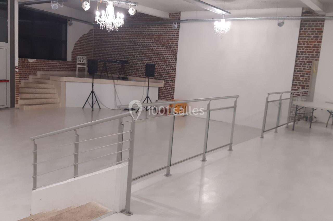 Location salle Tourcoing (Nord) - Latin Dance #8 Salle vide avec sol clair, murs en briques, rampe d'accès, estrade avec enceintes et éclairage suspendu.