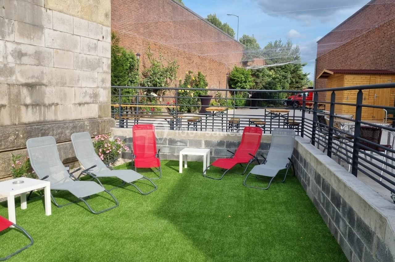 Location salle Tourcoing (Nord) - Latin Dance #16 Chaises longues rouges et grises disposées sur une terrasse en gazon synthétique, entourée de murs et de balustrades.