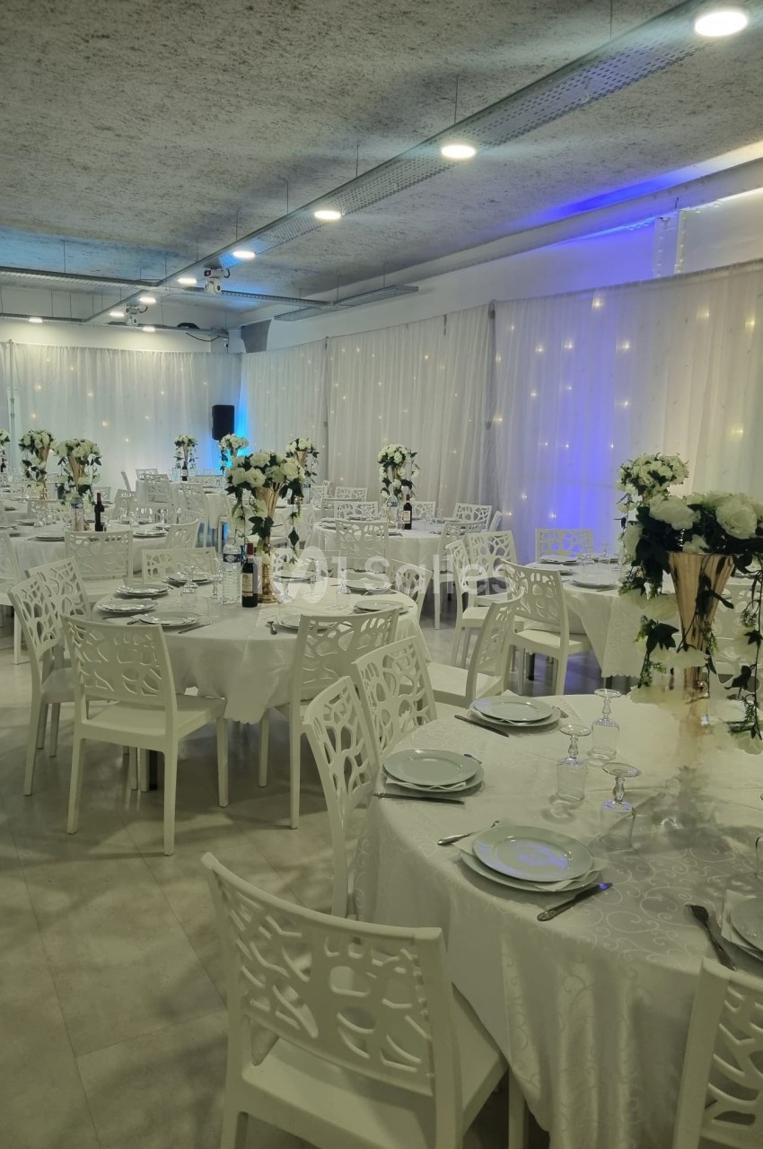 Salle de réception décorée avec des tables rondes, nappes blanches, chaises ajourées et centres de table fleuris.