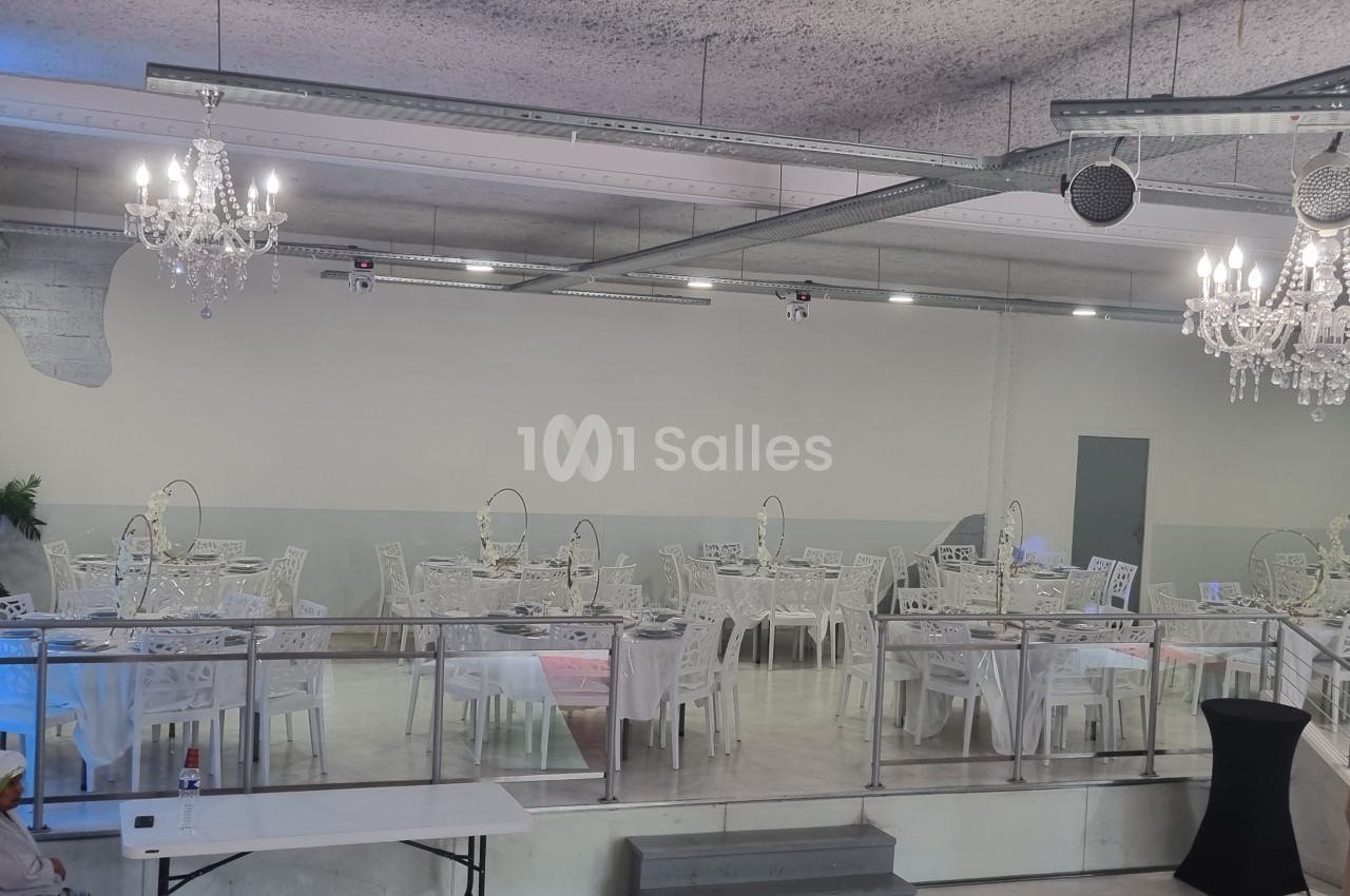 Salle de réception avec tables dressées, chaises blanches et lustres suspendus dans un décor moderne et épuré.