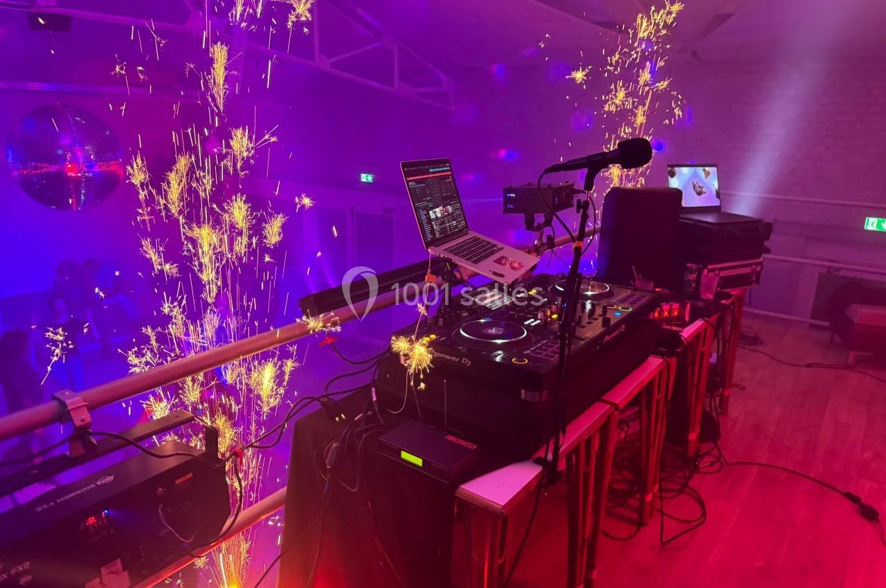 Location salle Tourcoing (Nord) - Latin Dance #19 Poste de DJ avec platines et ordinateur, entouré d'effets pyrotechniques dans une salle éclairée par des lumières colorées.