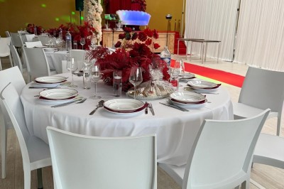 Salle de réception décorée avec des tables blanches, des colonnes fleuries et un tapis rouge menant à une estrade.
