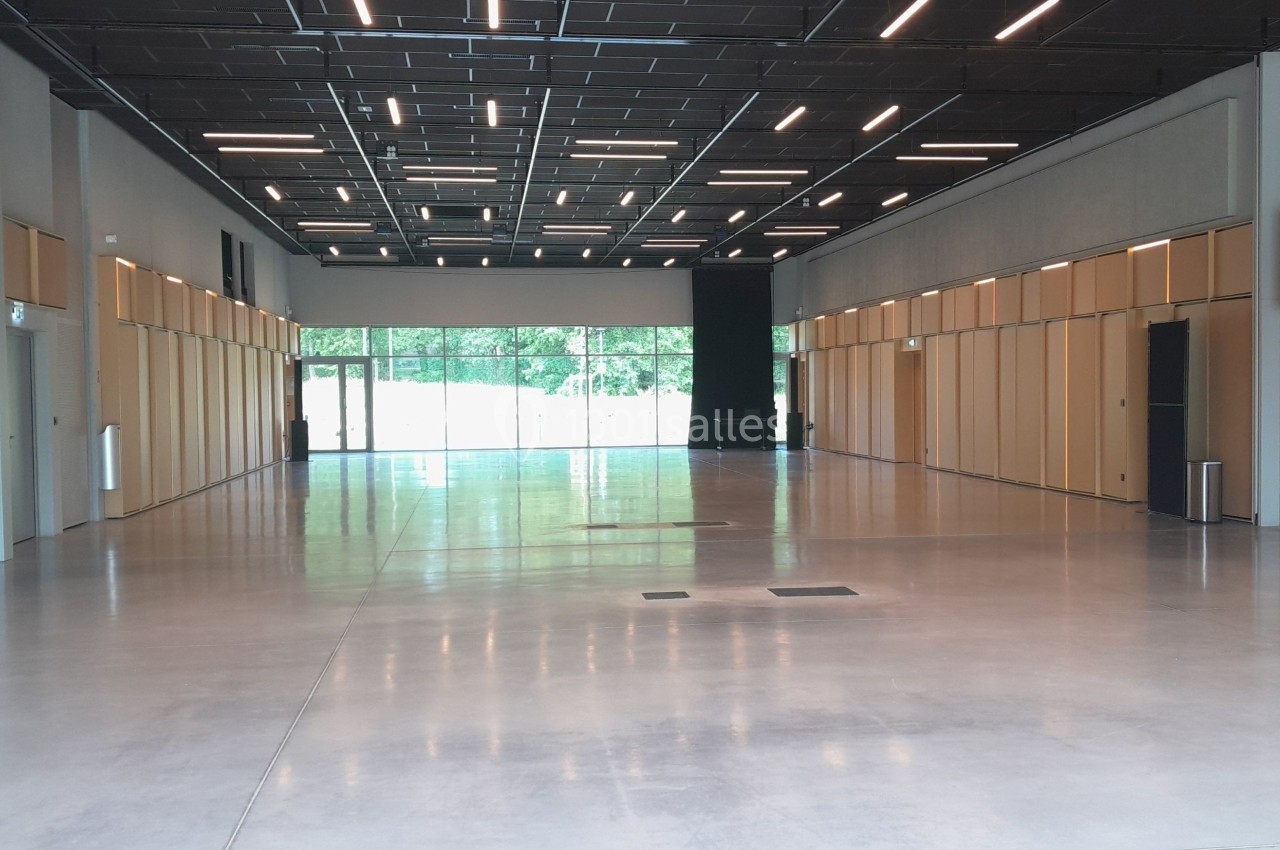 Salle spacieuse avec sol en béton, murs clairs, panneaux en bois et plafond noir équipé de luminaires modernes.
