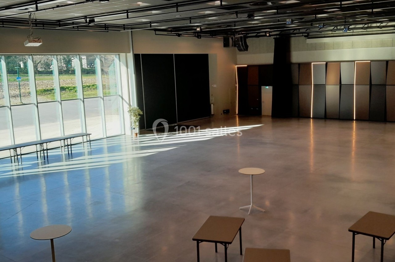 Salle spacieuse avec sol en béton, grandes baies vitrées laissant entrer la lumière et mobilier minimaliste.