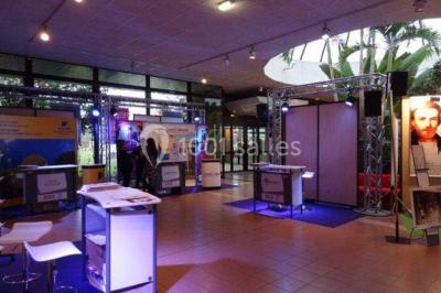 Salle de réception avec tables rondes dressées, éclairage coloré et scène équipée pour un événement.