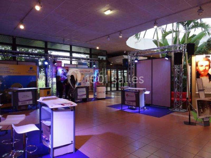 Salle d'exposition avec stands éclairés, panneaux d'affichage et quelques visiteurs en arrière-plan.