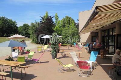 Salle de réception avec tables rondes dressées, éclairage coloré et scène équipée pour un événement.
