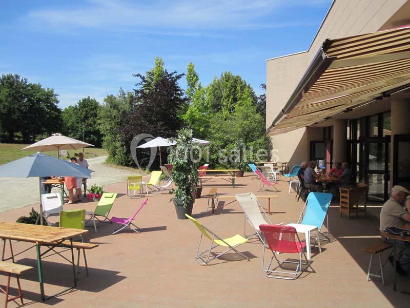 Terrasse ensoleillée avec chaises colorées, tables et parasols, entourée de verdure et fréquentée par des personnes.