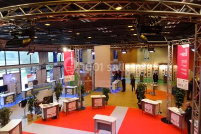 Salle de réception avec tables rondes dressées, éclairage coloré et scène équipée pour un événement.