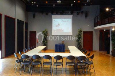 Salle de réception avec tables rondes dressées, éclairage coloré et scène équipée pour un événement.