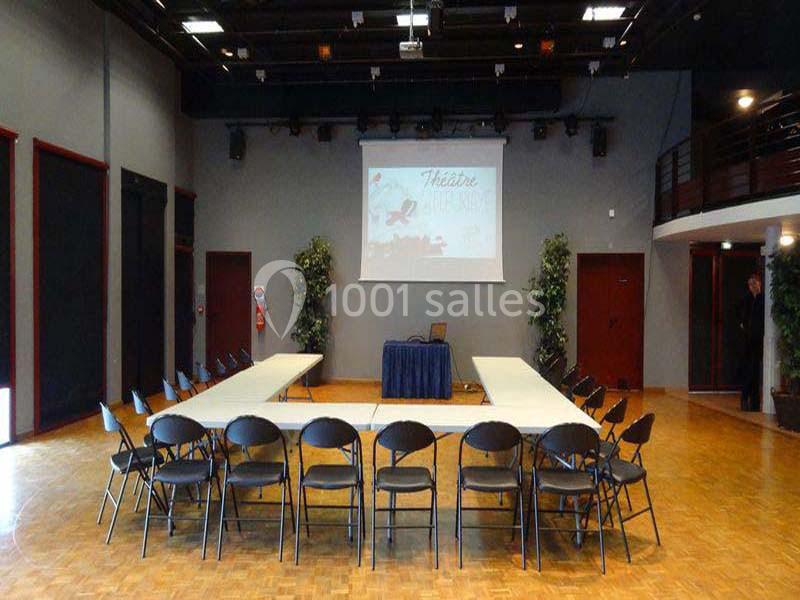 Salle de réunion avec des tables disposées en U, des chaises pliantes et un écran de projection en arrière-plan.