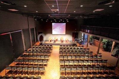Salle de réception avec tables rondes dressées, éclairage coloré et scène équipée pour un événement.