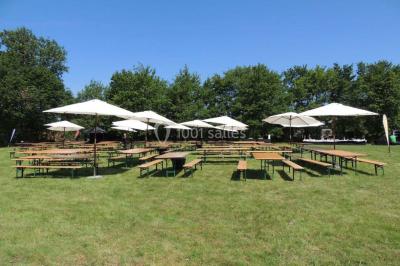 Salle de réception avec tables rondes dressées, éclairage coloré et scène équipée pour un événement.