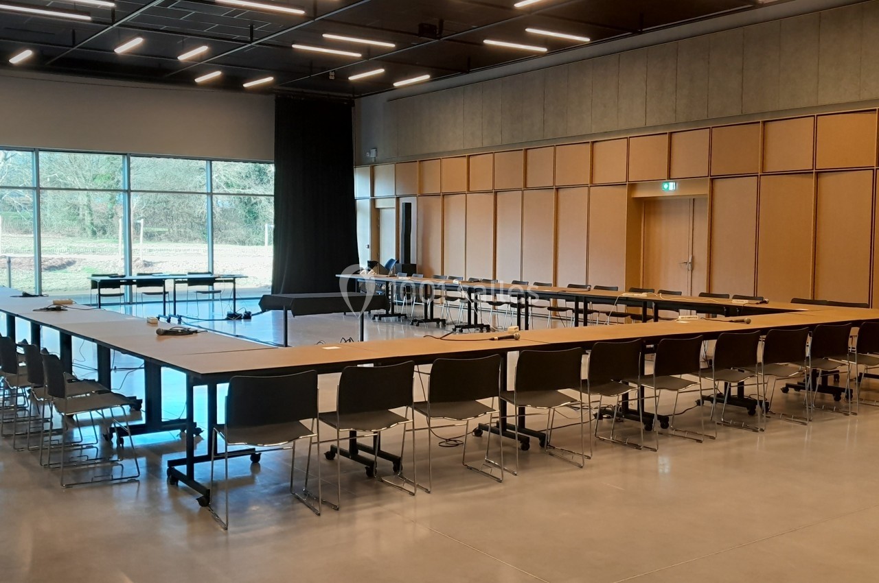 Salle de réunion lumineuse avec une grande table en U entourée de chaises, vue sur l'extérieur à travers une baie vitrée.