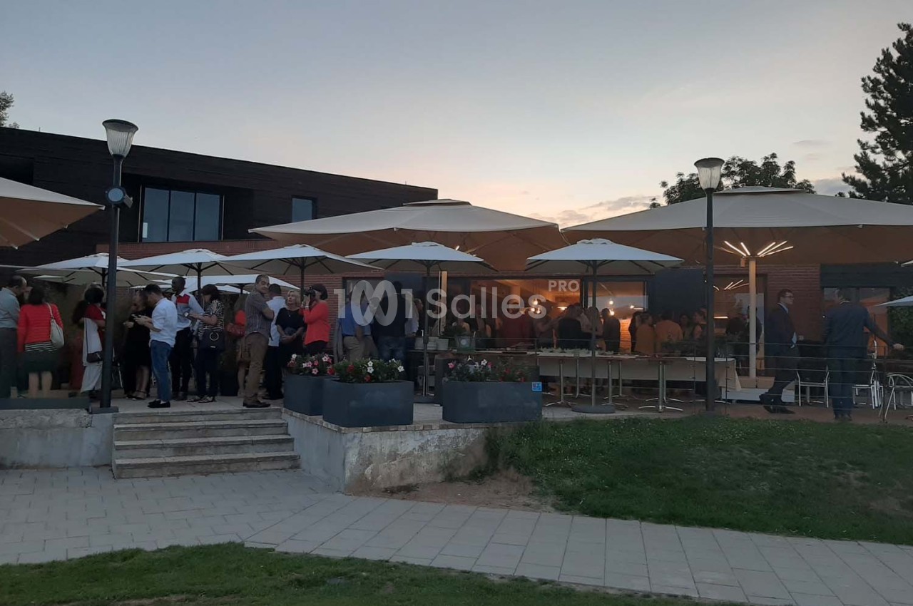 Groupe de personnes rassemblées sous des parasols sur une terrasse au crépuscule.